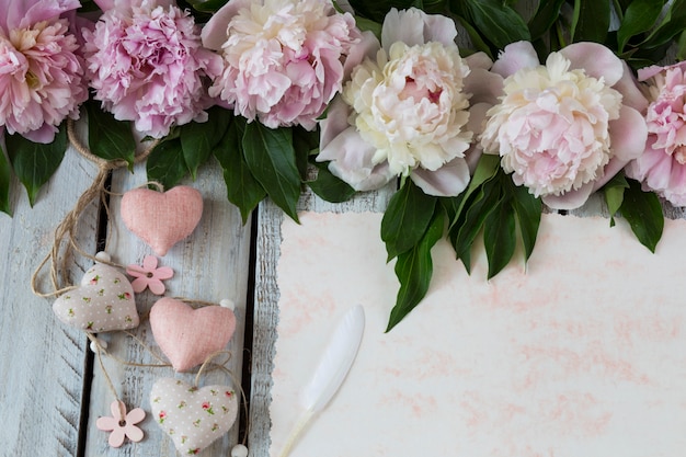 sur un fond en bois clair pivoines roses une feuille de vieux papier avec une plume et des coeurs