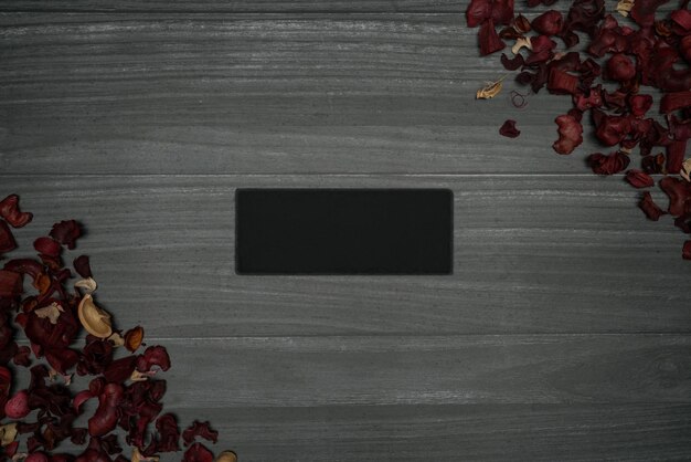 Photo fond en bois gris avec petite plaque de pierre rectangulaire et feuilles sèches rouges