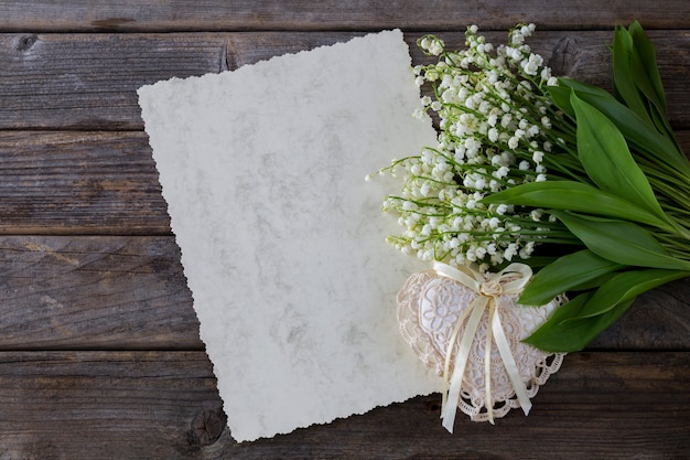 sur un fond en bois muguet, une feuille de papier et un coeur de dentelle