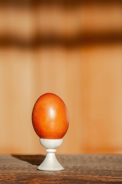 sur un fond en bois, un œuf de Pâques peint en rouge se dresse sur un support avec des colorants naturels