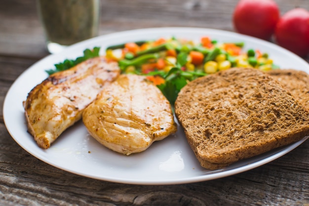 Sur un fond en bois, plaque blanche avec petit-déjeuner, poitrine de poulet et légumes