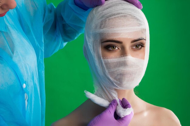 Sur fond de chromakey, le médecin avec des gants lie la femme avec un bandage