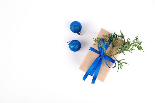 sur fond clair un cadeau avec un ruban bleu une branche de sapin et des ornements bleus