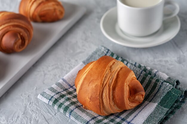 Sur un fond clair un croissant parfumé fraîchement sorti du four avec une tasse de lait