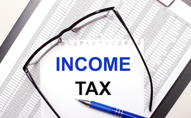 Sur un fond clair un rapport blackframed lunettes un stylo et une feuille de papier avec le texte de l'impôt sur le revenu concept d'entreprise