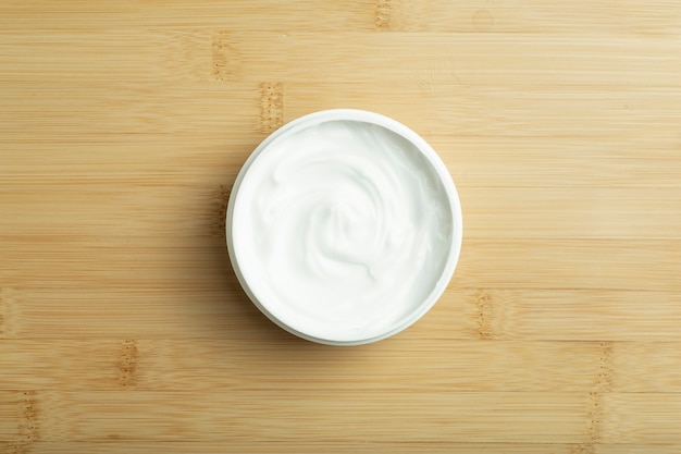 Fond de crème cosmétique crème cosmétique blanche pour la peau et le corps dans un pot blanc ouvert sur une ba...