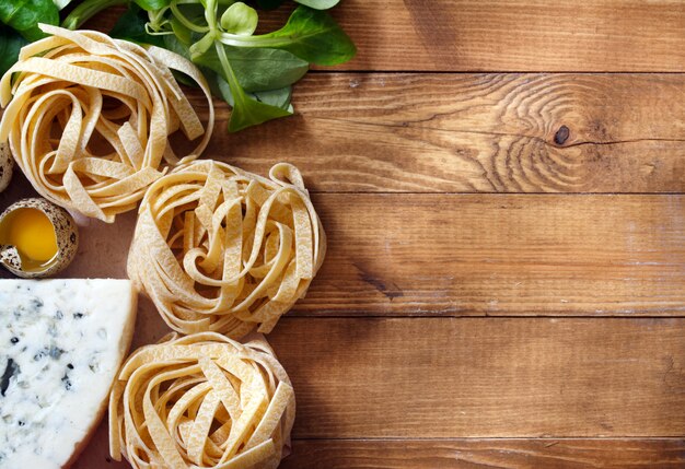 Fond de cuisine italienne sur des planches en bois rustique avec fond, avec des pâtes tagliatelles, des tomates, du basilic, du fromage, des grossini et des condiments