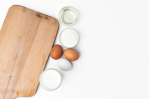 Fond de cuisson avec des œufs crus et une planche à découper en bois sur blanc