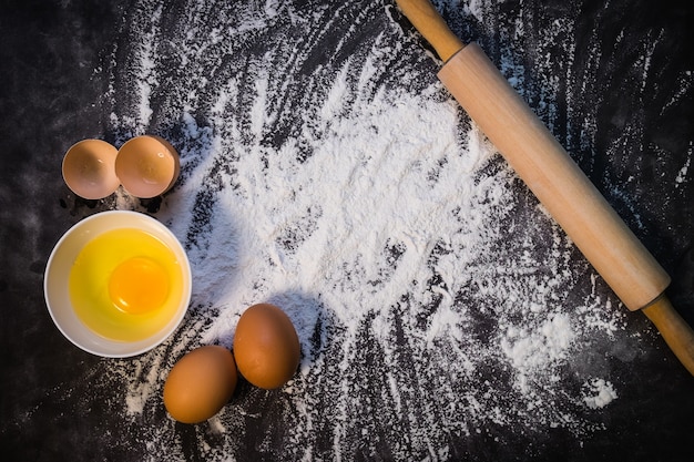 Fond de cuisson avec le rouleau à pâtisserie avec de la farine. Sur la table noire