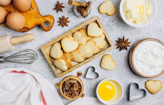 Fond culinaire de la Saint-Valentin. Ingrédients pour cuisiner sur table de cuisine en bois, recette de pâtisserie. Biscuits en forme de coeur. Vue de dessus. Mise à plat.