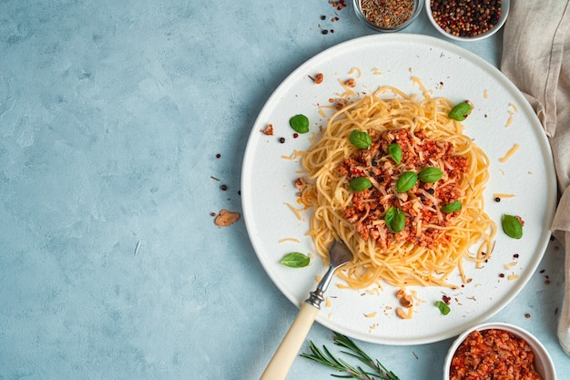 Fond culinaire avec spaghetti et sauce bolognaise sur fond bleu-gris.