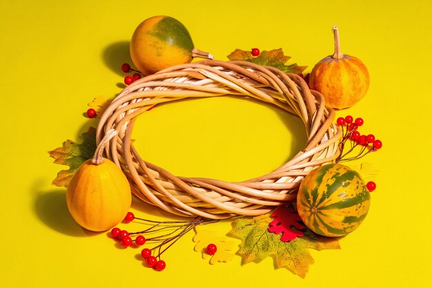 Fond de décoration d'automne avec des citrouilles, des feuilles et des baies. Couronne tressée sur fond pastel jaune vif, espace pour copie