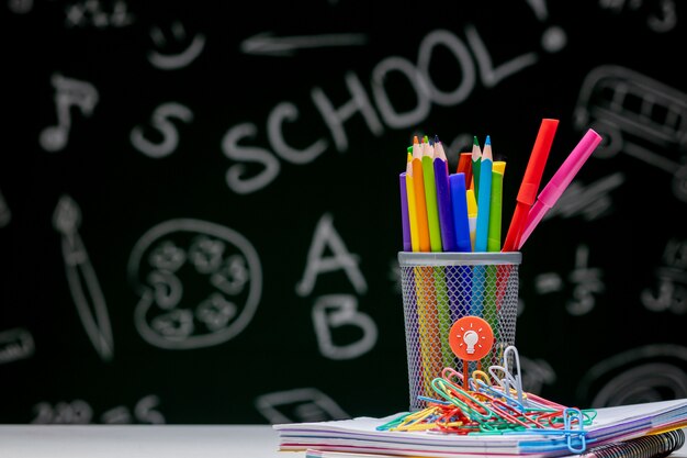 Fond d'école avec des accessoires de papeterie. Livres, globe, crayons et diverses fournitures de bureau allongé sur le bureau sur un fond de tableau noir vert