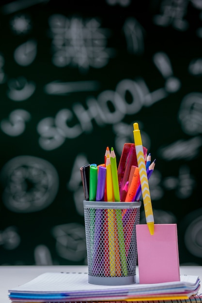 Fond d'école avec des accessoires de papeterie. Livres, globe, crayons et diverses fournitures de bureau allongé sur le bureau sur un fond de tableau noir vert