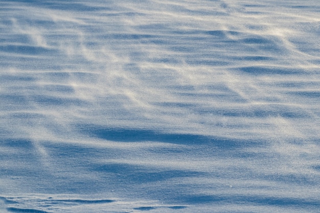 Fond enneigé, surface enneigée de la terre après un blizzard le matin au soleil avec des couches distinctes de neige