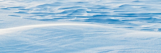 Fond enneigé, surface enneigée de la terre après un blizzard le matin au soleil avec des couches distinctes de neige