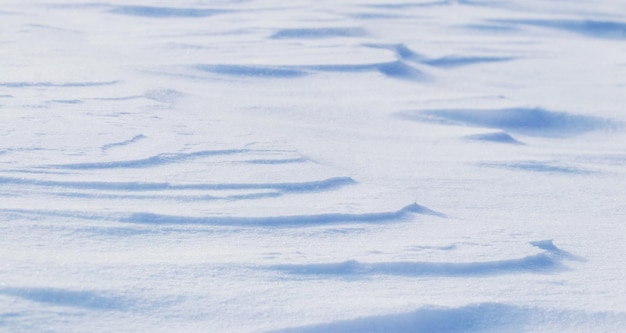 Fond enneigé, surface enneigée de la terre après un blizzard le matin au soleil avec des couches distinctes de neige