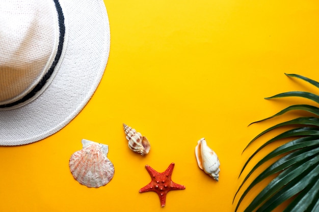 Fond d'été avec coquillages, chapeau de plage et feuille de palmier sur fond jaune. Été, vacances à la plage et concept de voyage