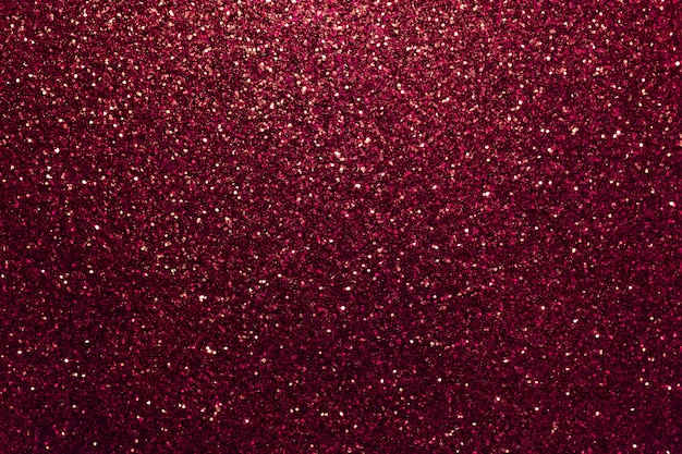 Fond étincelant rouge foncé de petits paillettes, gros plan. Toile de fond brillante.