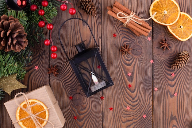 Fond festif de noël avec lanterne chandelier sapin de noël décoré avec un cadeau de pomme de pin enveloppé dans du papier kraft oranges séchées sur fond en bois espace de copie plat