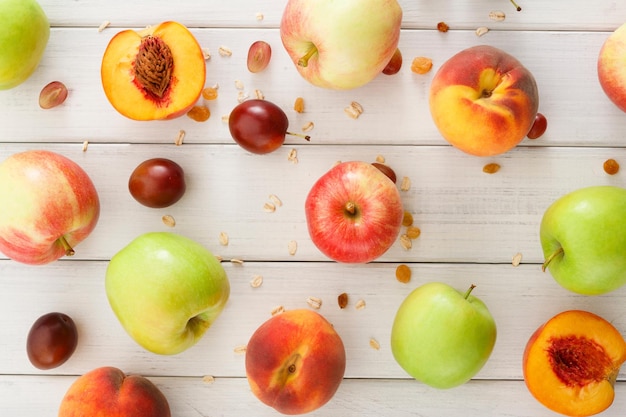 Fond de fruits de saison sains. Beaucoup de pommes mûres, pêches et prunes, flocons d'avoine et raisins secs sur la vue de dessus de table en bois blanc, motif, concept de récolte d'automne