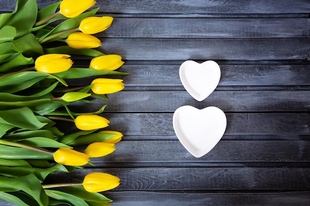 Sur un fond gris en bois se trouvent des tulipes jaunes et des soucoupes en forme de chiffre huit