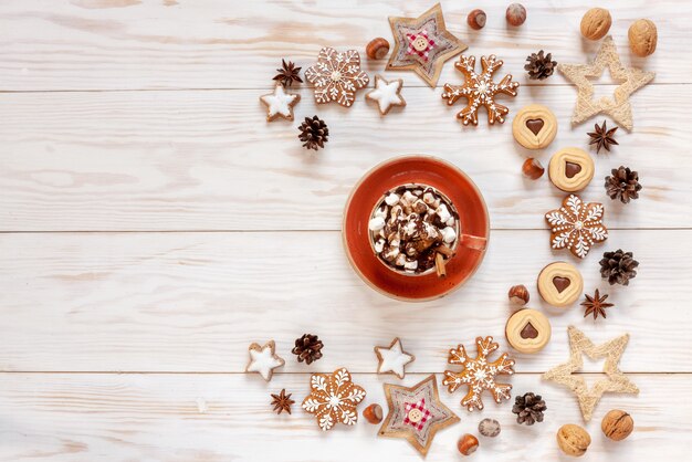 Fond de guirlande de vacances de Noël avec biscuits maison, boisson chaude à la guimauve, tranches d'orange séchées, noix, épices et cônes