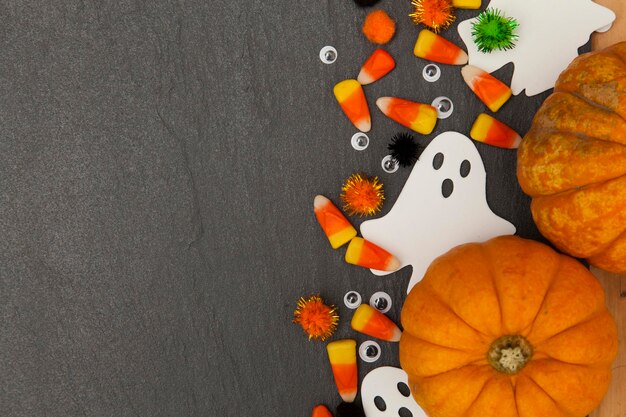 Fond d'Halloween avec des fantômes et des bonbons au maïs sur un fond d'ardoise