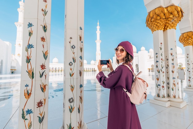 Sur le fond de l'impressionnante Grande Mosquée du Cheikh Zayed, une touriste à Abaya prend des photos et des vidéos.