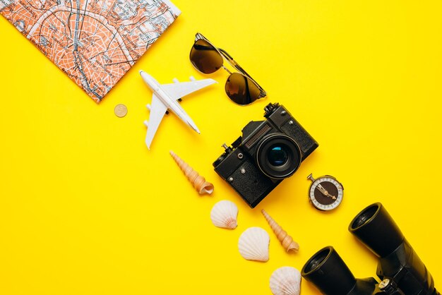 Photo sur un fond jaune sur une diagonale des choses importantes sont disposées lunettes de soleil jumelles la caméra la carte l'avion la boussole