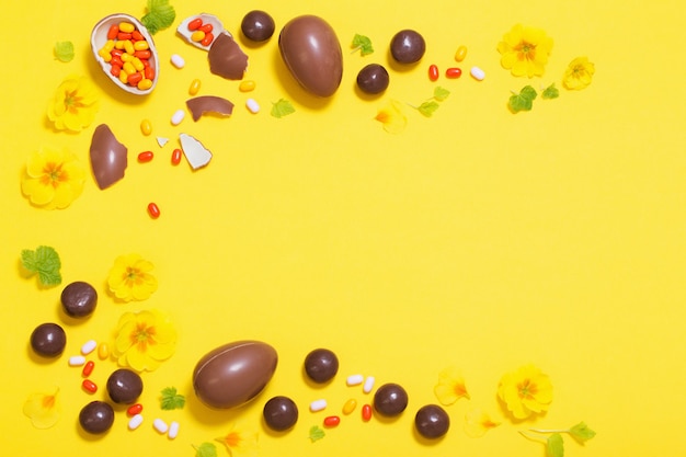 Fond jaune de Pâques avec des œufs en chocolat, des bonbons et des spri