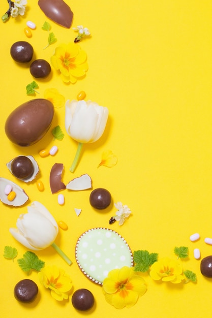 Fond jaune de Pâques avec des œufs en chocolat, des bonbons et des spri