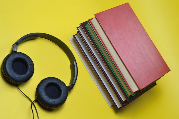 Photo sur fond jaune, une pile de livres et de gros écouteurs noirs.