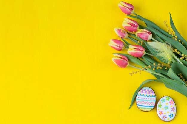 sur fond jaune tulipes, mimosa, plume et deux pains d&#39;épice en forme d&#39;oeufs de pâques