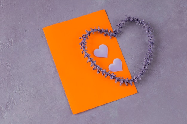 Sur un fond lilas, une feuille de papier orange, deux coeurs en satin et un coeur de lavande