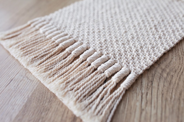 Fond de macramé beige fait à la main. Texture macramé, tricot écologique et moderne. Tapis en macramé sur table en bois