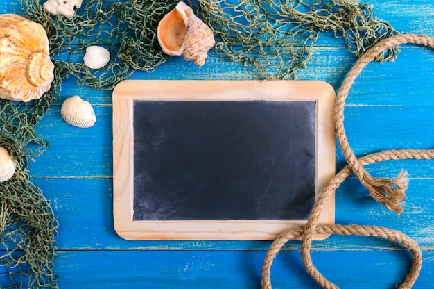 Fond de mer tropicale. Différentes coquilles, vieux filet de pêche sur les planches bleues, vue de dessus. Espace libre pour les inscriptions sur l'ardoise. Thème d'été.