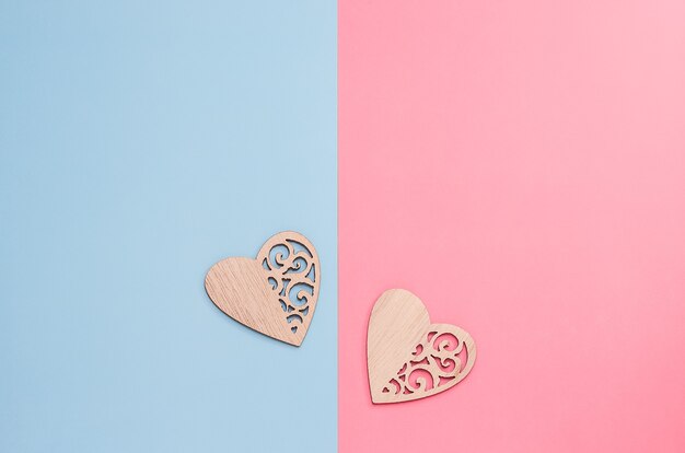 Fond de minimalisme pour la Saint-Valentin, deux coeurs sculptés en bois sur fond rose-bleu avec espace de copie.