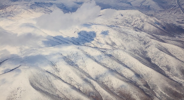 Fond de montagnes enneigées et nuages blancs au-dessus d'eux Photo aérienne de la fenêtre de l'avion