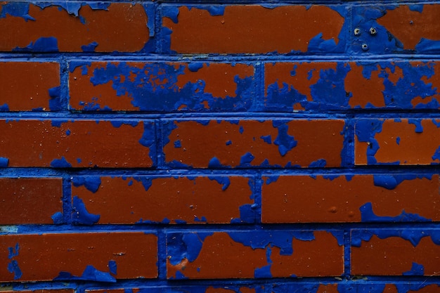 Fond de mur coloré avec des peintures endommagées de bleu sur des briques rouges