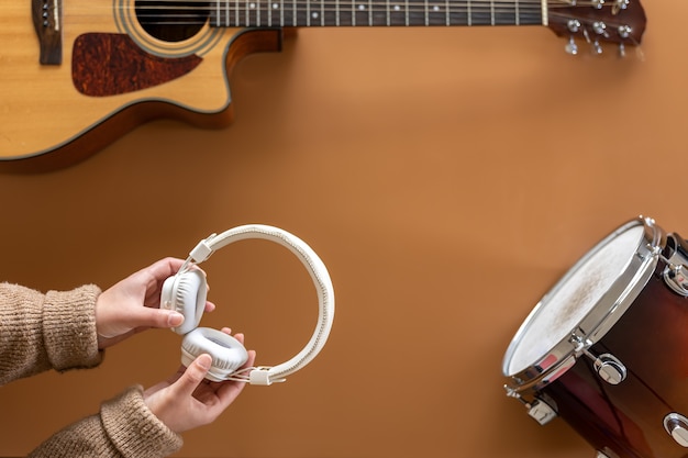 Fond musical avec une guitare, des tambours et des écouteurs dans des mains féminines, le processus de création de musique, vue de dessus.