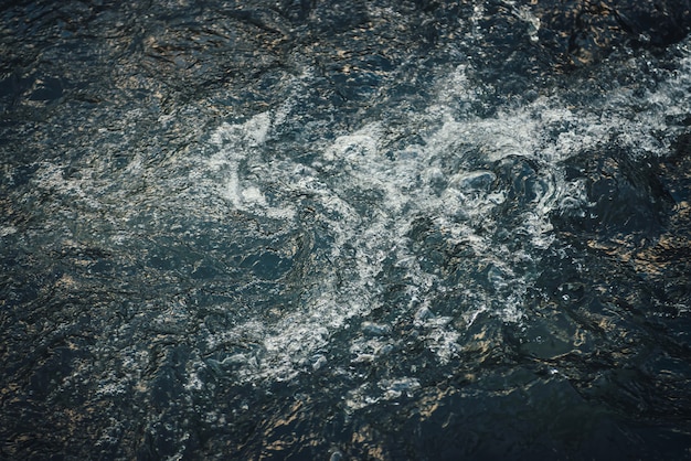 Fond de nature atmosphérique de l'eau dorée de la rivière de montagne au lever ou au coucher du soleil. Fragment pittoresque de la surface de l'eau avec reflet du soleil doré. La lumière du soleil se reflète dans le jet d'eau bleu doré.