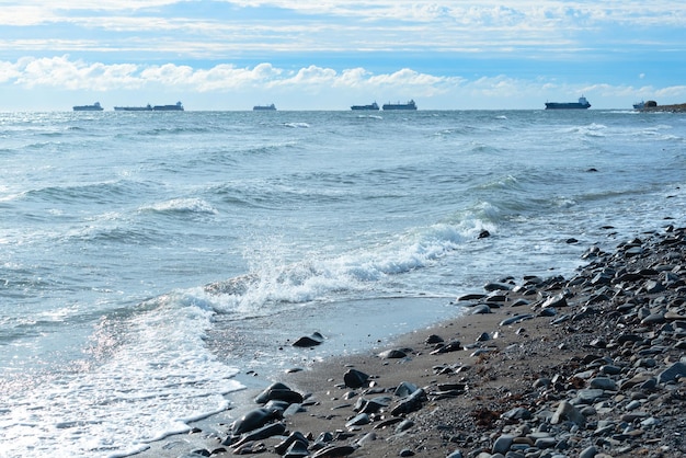 Fond de nature avec des vagues de la mer frappant le bord de la mer Vue panoramique de la mer contre un ciel nuageux avec des navires à l'horizon