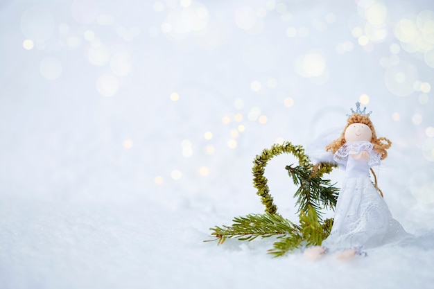 Fond de Noël ange de poupée, coeur fait de sapin sur la neige avec bokeh
