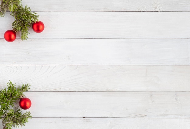 Fond de Noël en bois blanc avec des branches de sapin décorées de boules rouges, vue de dessus, espace pour copie