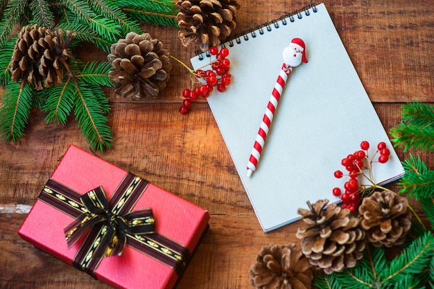 Fond de Noël. Branches d'épinette, baies rouges, cahier, cadeau et tasse avec des guimauves sur un fond en bois