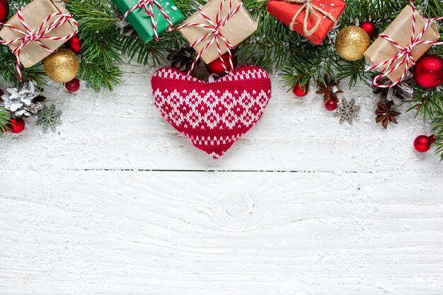 Fond de Noël avec des branches de sapin, coeur tricoté, décorations, coffrets cadeaux et pommes de pin