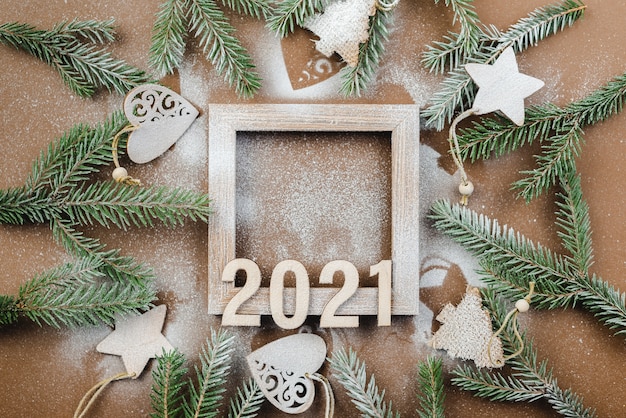Fond de Noël avec des branches de sapin et des ornements en bois 2021 sur une table marron.