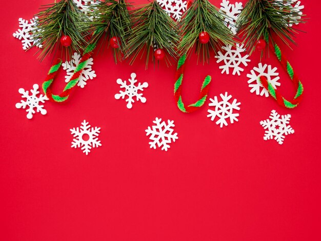 Fond de Noël. Une composition festive. Flocons de neige blancs, une branche d'épinette et une canne au caramel sur fond rouge. Vue de dessus, espace de copie, espace vide pour le texte.