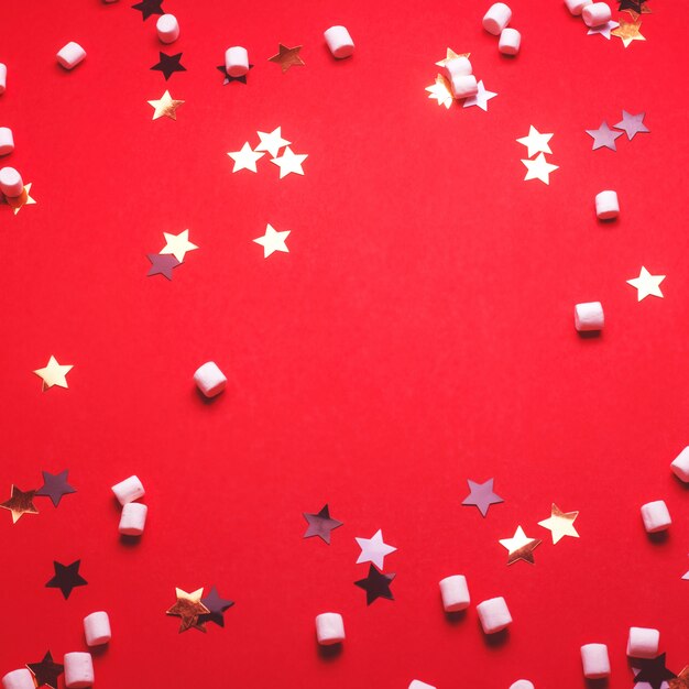 Fond de Noël avec des étoiles et des guimauves sur rouge.